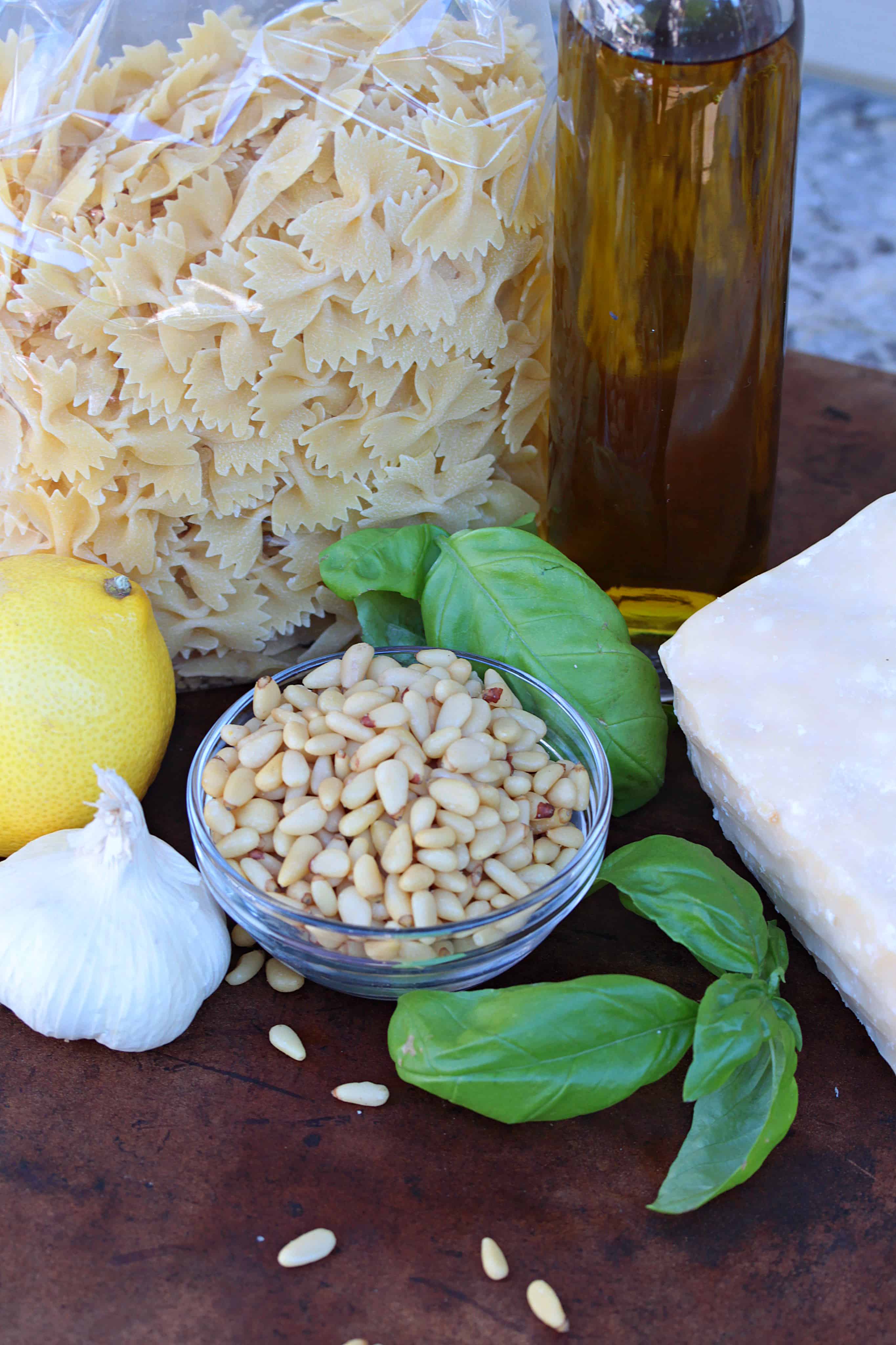 Ingredients for Bow Tie Pesto Pasta salad including olive oil, bow tie pasta, pine nuts, basil, parmesan, garlic and lemon