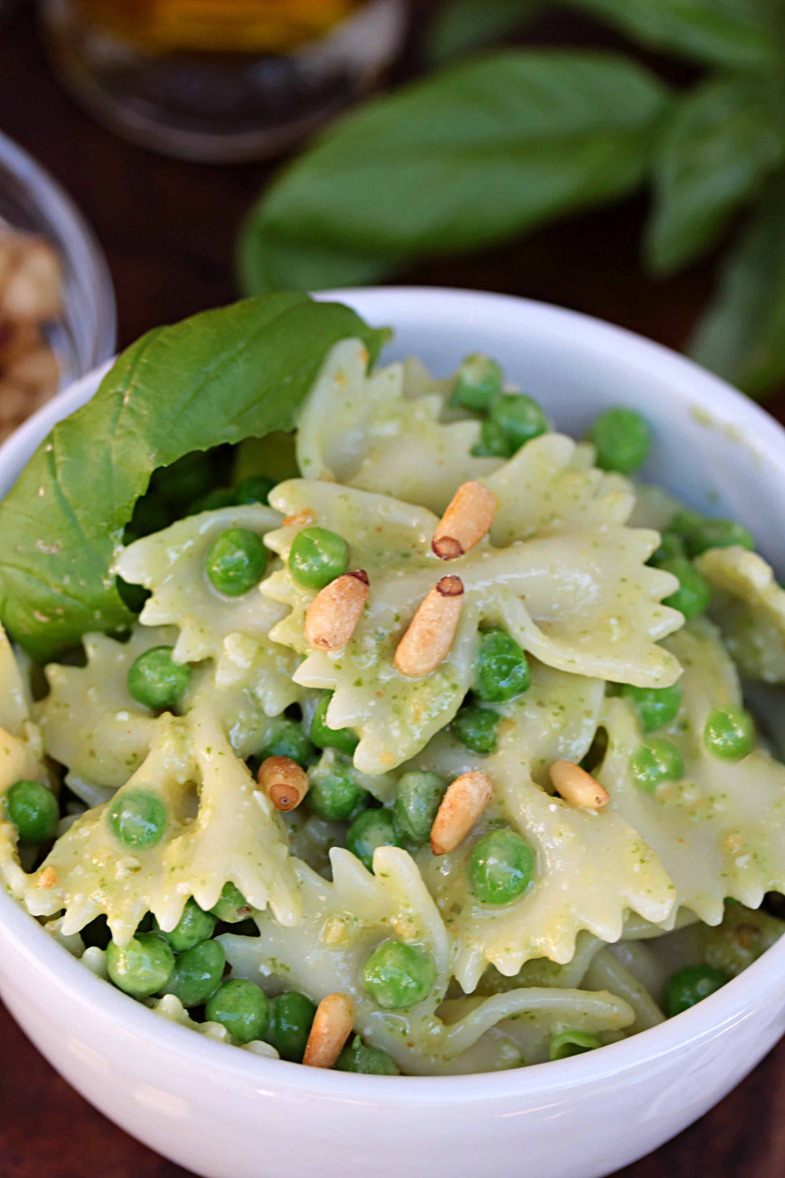 Bow Tie Pesto Pasta Salad in a white bowl with basil, pine nuts and peas