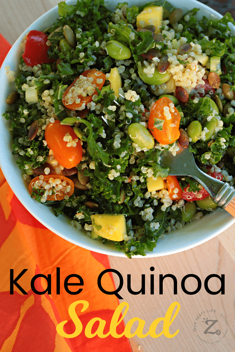 Taking a forkful of edamame Kale Quinoa Salad in a white bowl with tomatoes, quinoa, mangos and pepitas
