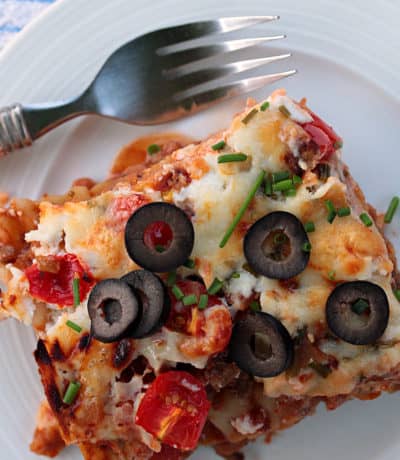 Mexican lasagna piece with olives on a white plate with a fork