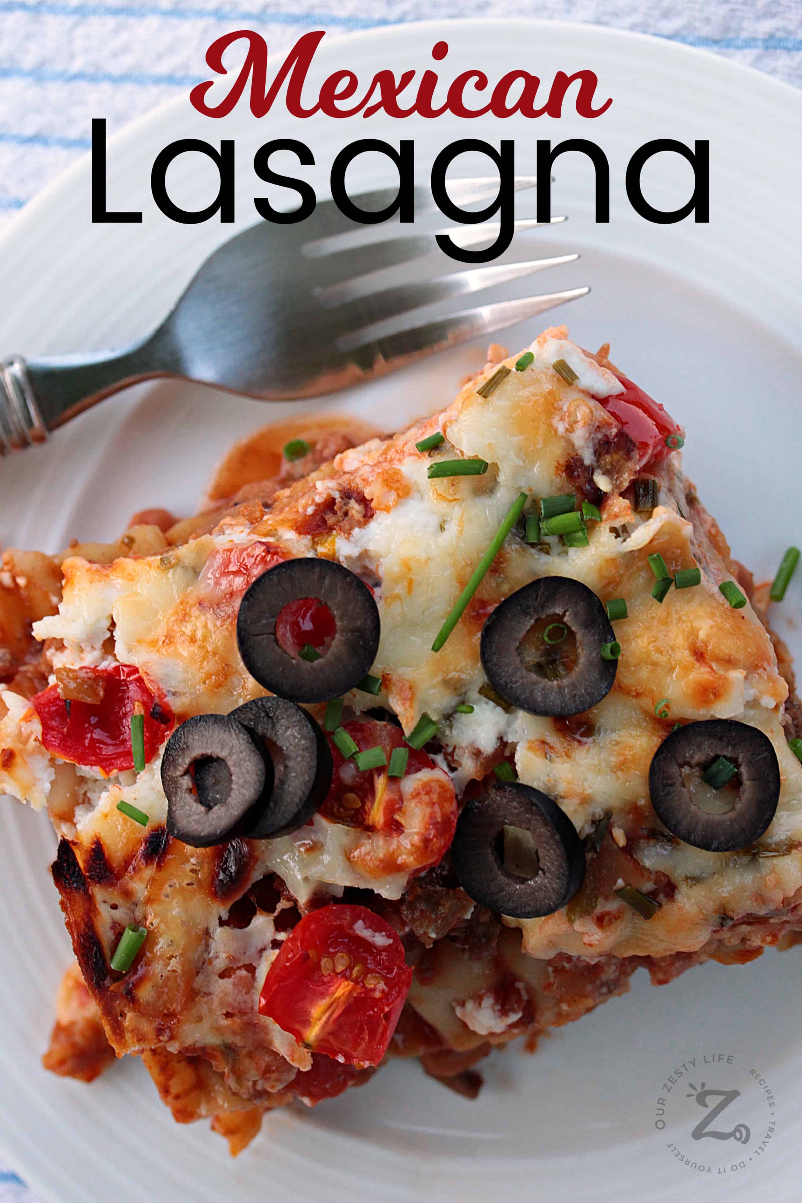 Mexican lasagna topped with olives and green onions on a white plate with a fork