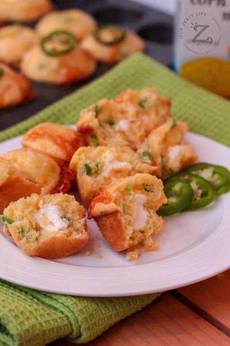 Mini Jalapeno Popper Corn Muffins with a cream cheese center and sliced jalapenos on the side on a white plate with a green towel and Mini Jalapeno Muffins in the background