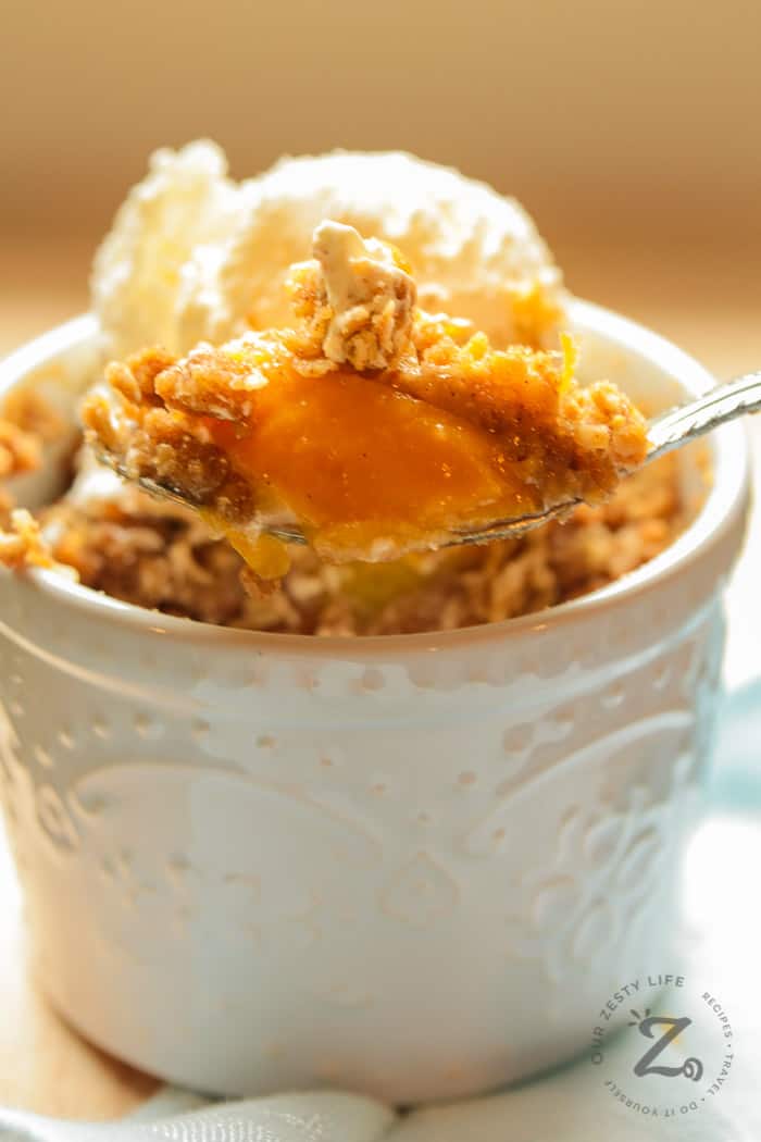 Easy Peach Crisp Recipe with peach crisp on a spoon with an individual easy peach crisp with ice cream in the background
