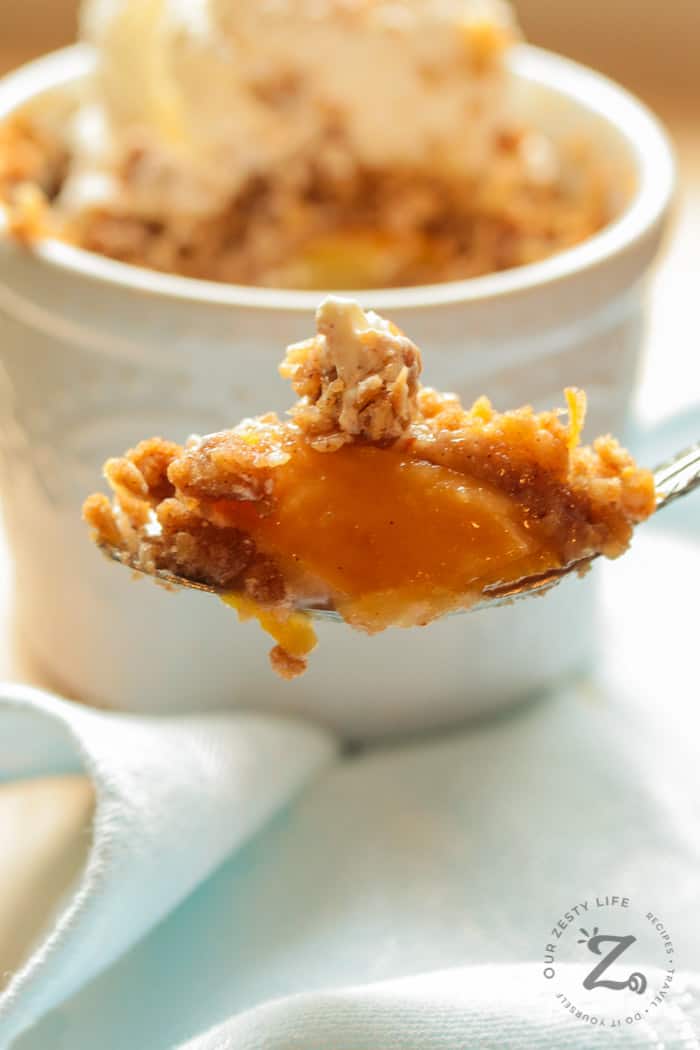 Peach Crisp Recipe with peach crisp and ice cream on a spoon with an individual easy peach crisp in the background