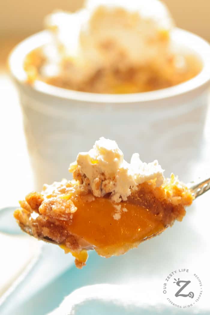 Easy Peach Crisp Recipe with peach crisp and ice cream on a spoon with an individual easy peach crisp in the background along with a light blue napkin