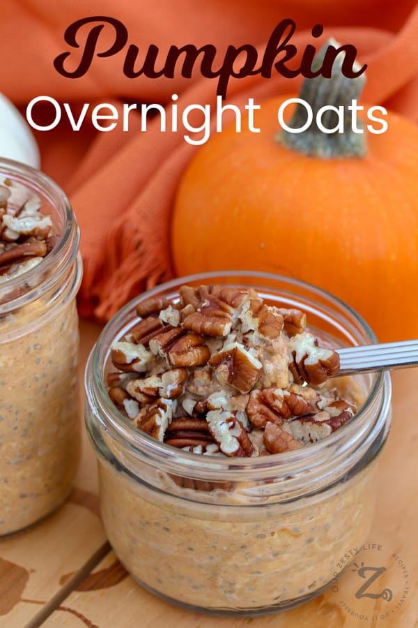 mason jars with pumpkin overnight oats topped with pecans, taking a spoonful from one, with a pumpkin in the background