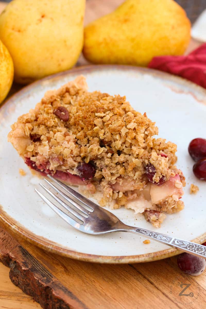 Cranberry Pear Pie on a plate with a fork with pears and cranberries in the background