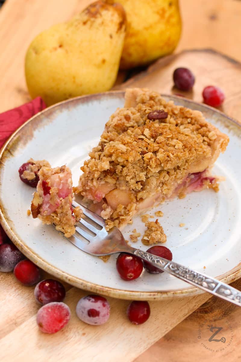 a slice of Cranberry Pear Pie on a plate with a fork with a bite on it, among pears and cranberries in the background