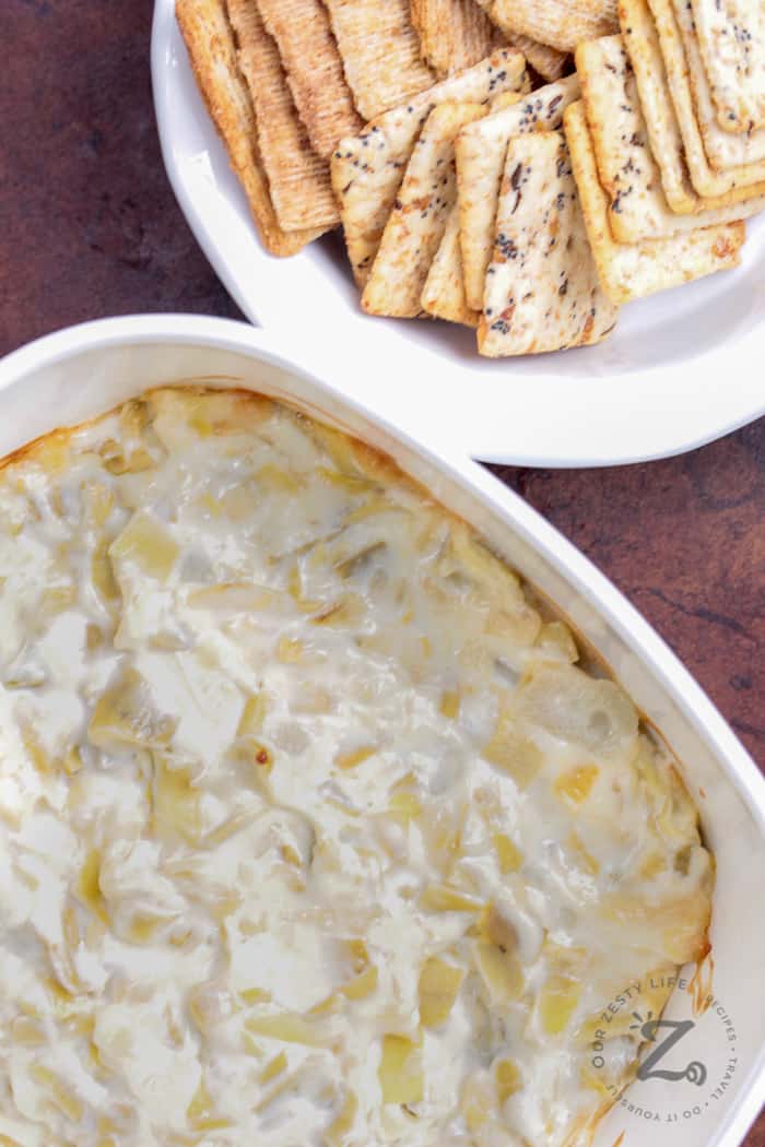 baked artichoke dip in a white casserole dish with crackers on the side