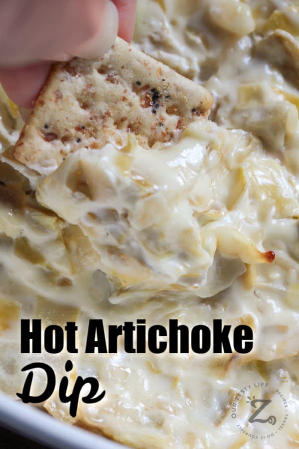 scooping hot artichoke dip with a cracker