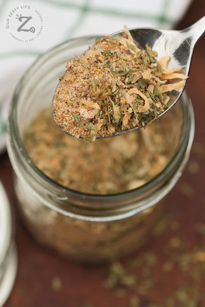 closeup of dry Italian dressing mix on a spoon with a glass jar filled with mix in the background