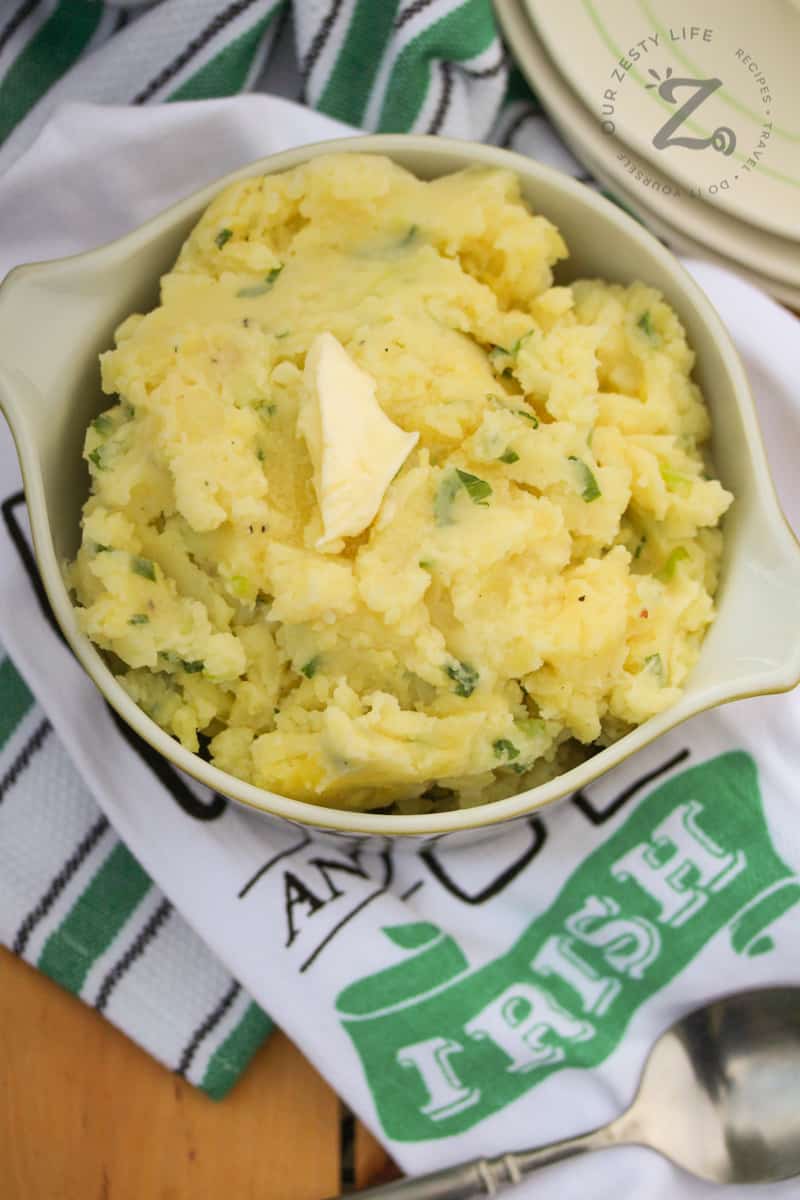 Irish Potato Recipe in a dish topped with a pat of butter with Irish teatowels in the background