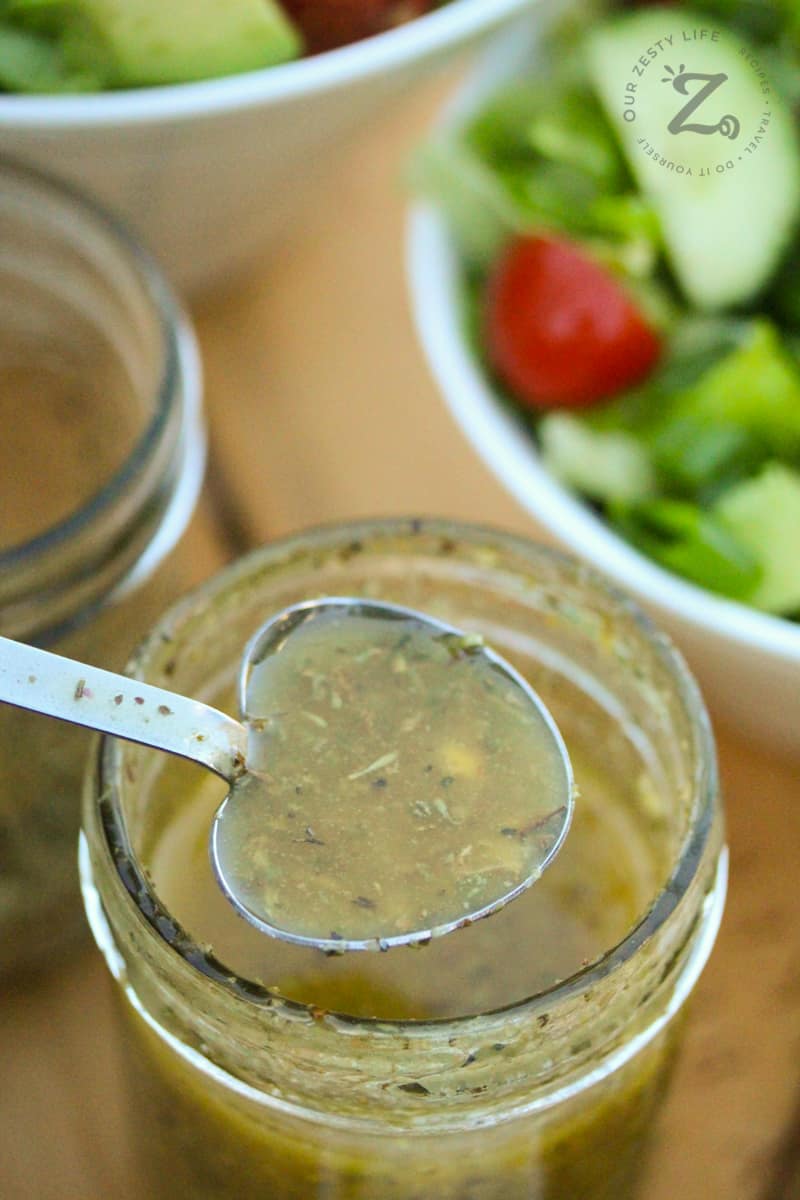 a spoonful of homemade Italian dressing with a mason jar filled with dressing and a salad in the background