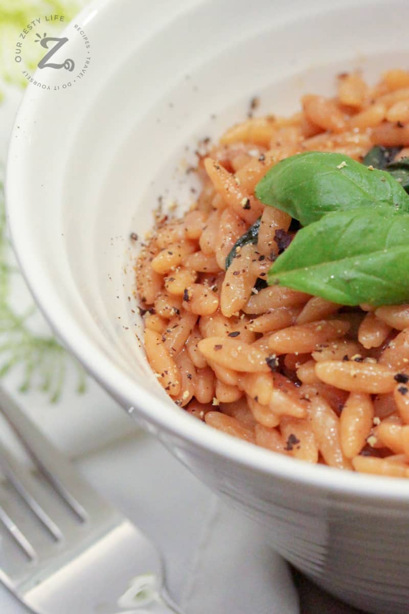 parmesan basil orzo in a white bowl garnished with pepper and basil, with a fork on the side