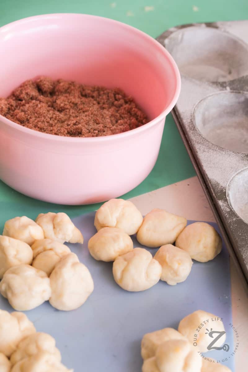 dough for monkey bread from scratch rolled into balls, with a pink bowl filled with cinnamon sugar mixture, and a prepared muffin tin