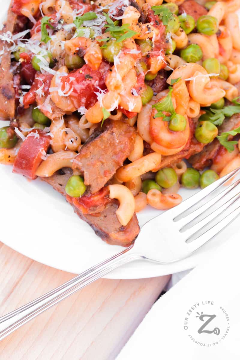 hamburger pasta with leftover hamburger patties, sausage, peas on a white plate with a fork