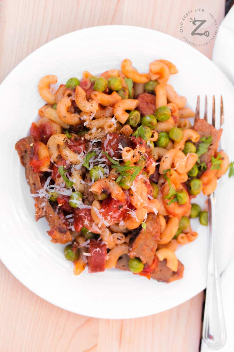 overhead of hamburger and pasta with leftover hamburger patties, sausage, peas on a white plate with a fork