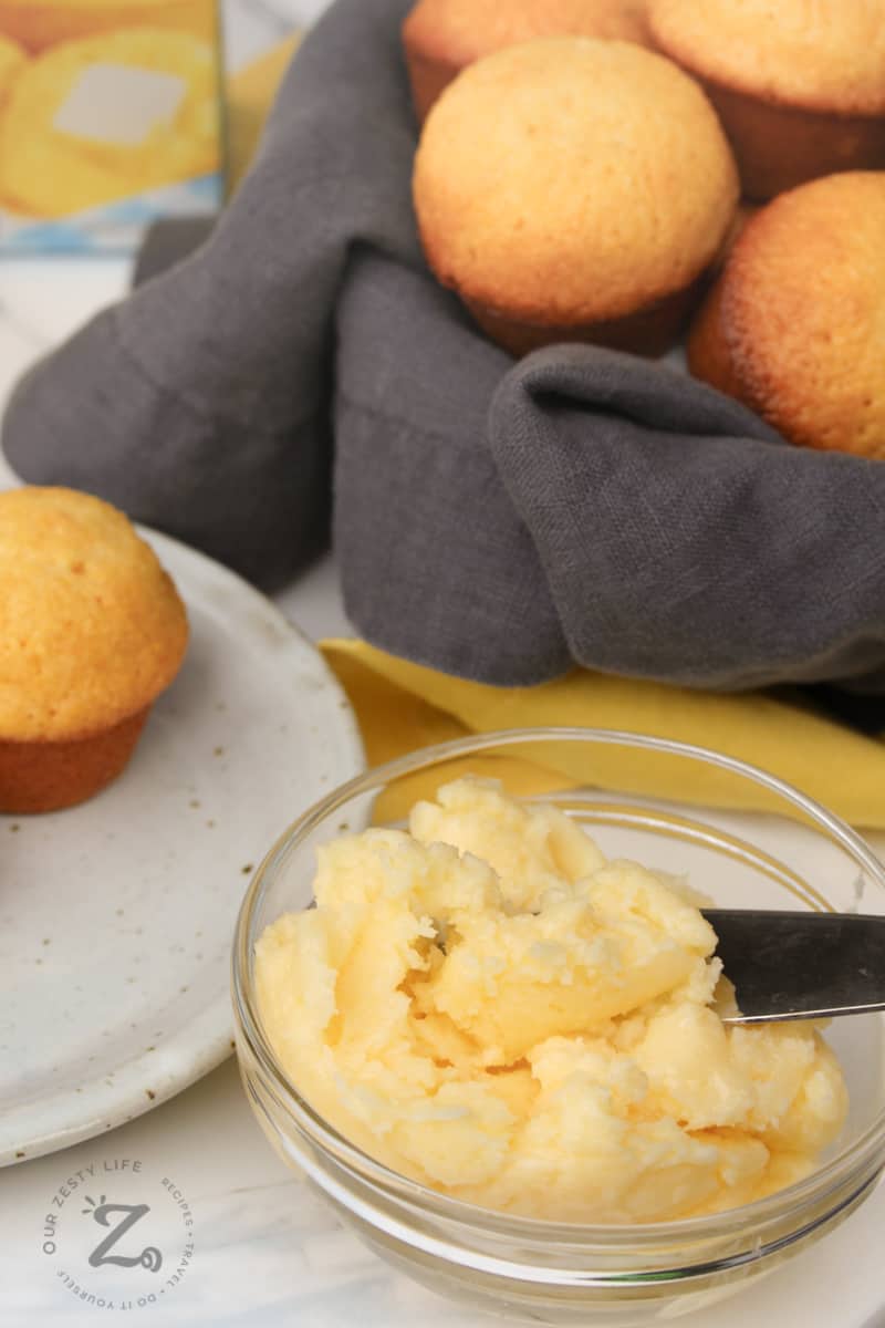 honey butter in a clear bowl with honey cornbread muffins in a basket and on a white plate