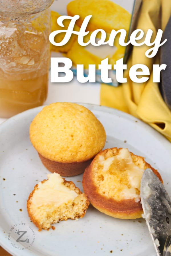 honey butter being spread on honey cornbread muffins on a white plate with a honey jar in the background