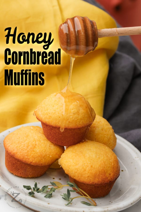 four honey cornbread muffins on a white plate, with honey being drizzled over the top with a honey dipper