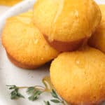 four honey cornbread muffins on a white plate, with honey drizzled over the top