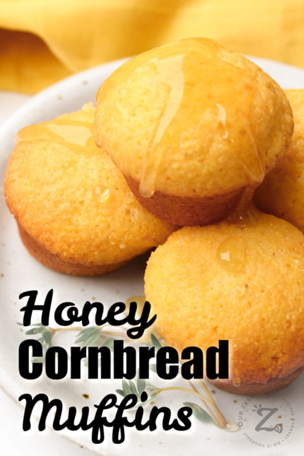 four honey cornbread muffins on a white plate, with honey drizzled over the top