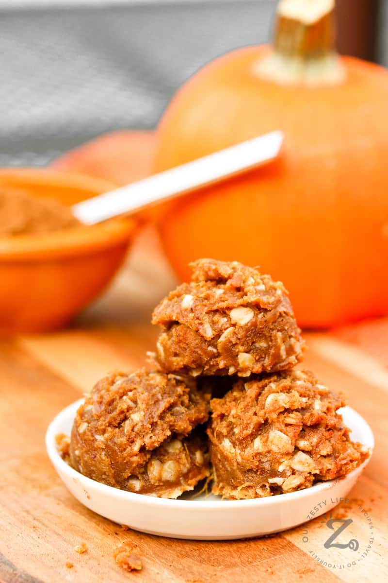 3 pumpkin energy balls on a white plate with a pumpkin in the background