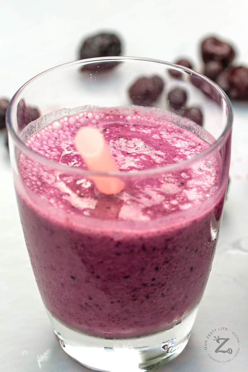 Close up of mixed berry smoothie in a glass with a straw and berries in the background