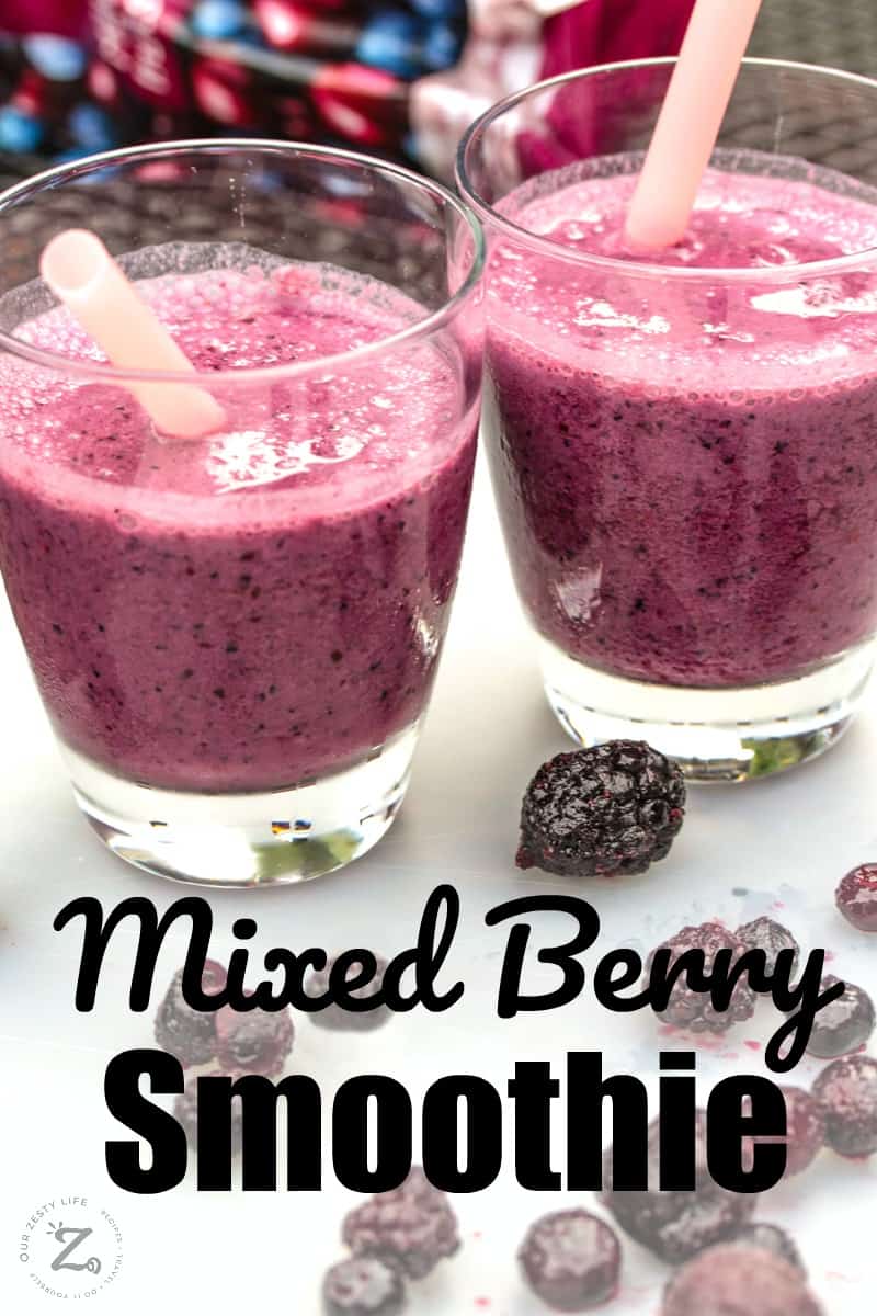 Overhead of two glasses of mixed berry smoothie with straws and berries in the on the table and a bag of frozen berries in the background