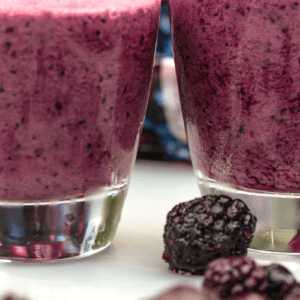 Two glasses of mixed berry smoothie with straws and berries in the on the table