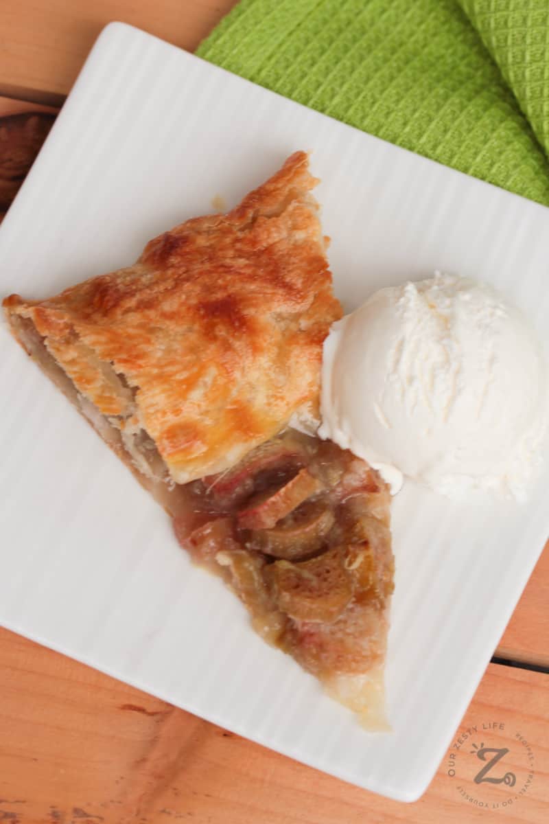 a slice of baked rhubarb galette (easy rhubarb pie on puff pastry) with a scoop of vanilla ice cream on a white plate