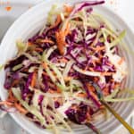 overhead of creamy coleslaw with carrots and cabbage in a large white bowl with tongs in it