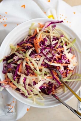 overhead of creamy coleslaw with carrots and cabbage in a large white bowl with tongs in it