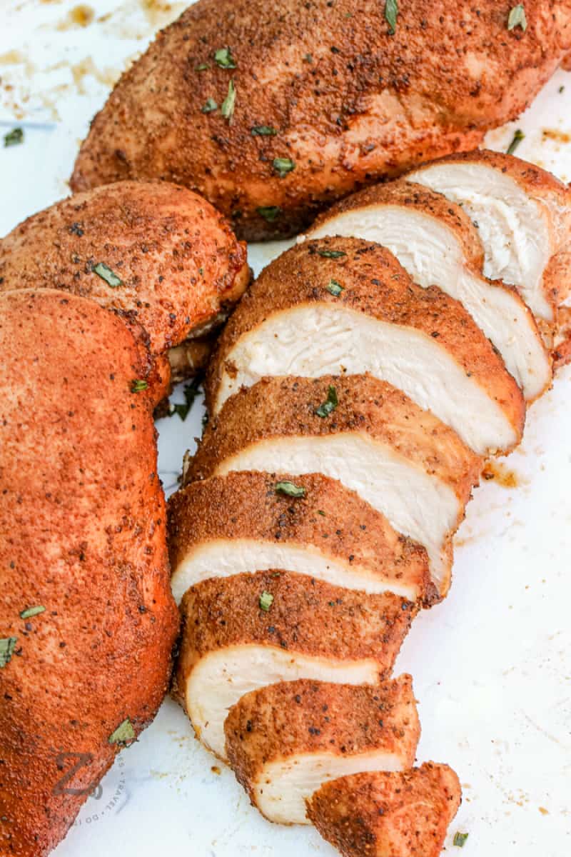 sliced smoked chicken breast with whole chicken breast on a white cutting board