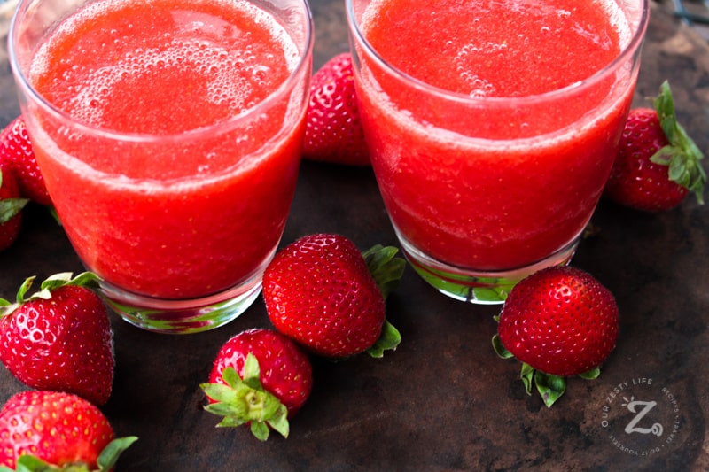 two glasses of homemade strawberry margarita recipe with fresh strawberries around them