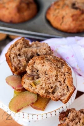 tender rhubarb applesauce muffins and some rhubarb slices on a white plate with muffins in a tin in the background