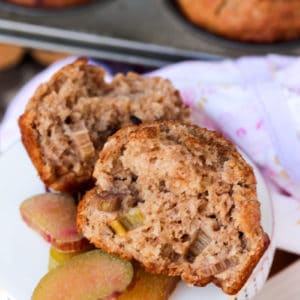 tender rhubarb applesauce muffins and some rhubarb slices on a white plate with muffins in a tin in the background