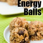 three peanut butter energy balls with chocolate chips on a white plate with a plate of energy bites in the background