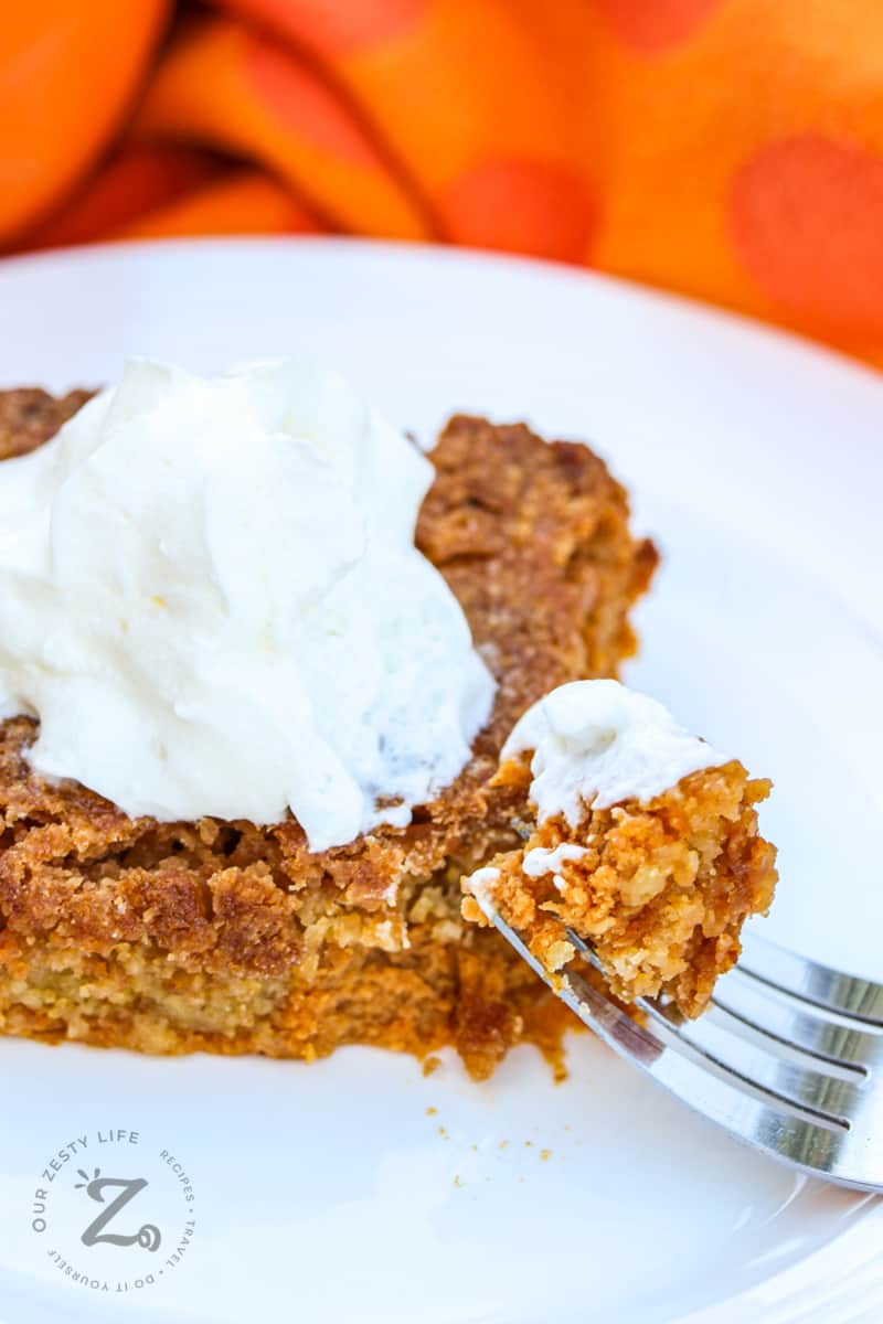 a square of pumpkin pie crunch on a plate with a scoop of ice cream on top with a fork with a bite of pumpkin pie crunch in the foreground
