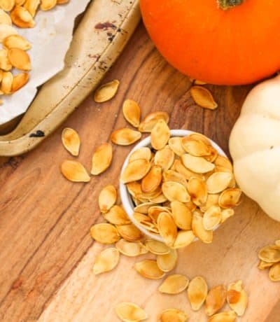 Roasted Pumpkin Seeds in a bowl with pumpkins and a baking tray on the side