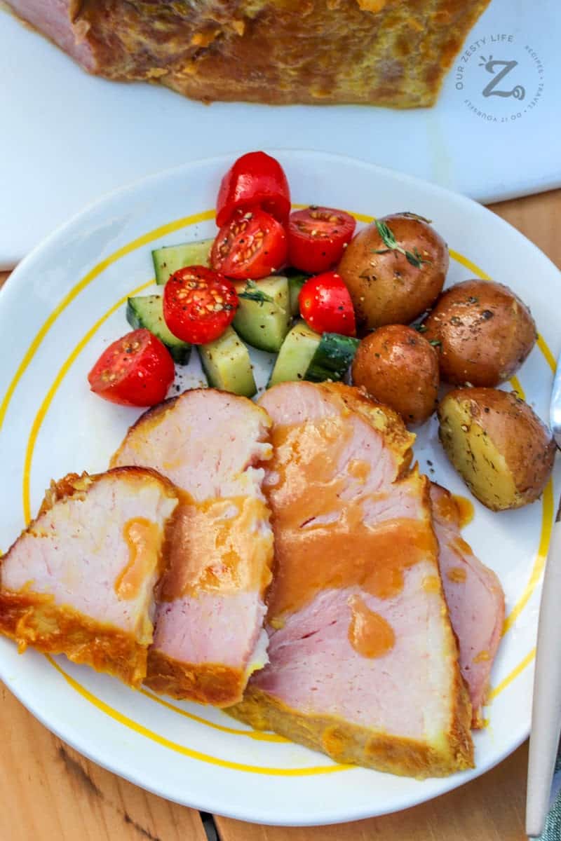 oven baked ham with pineapple glaze on a white plate with roasted potatoes and tomato cucumber salad