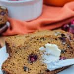 Pumpkin Cranberry Bread slices with butter with cranberries and pumpkin in the background