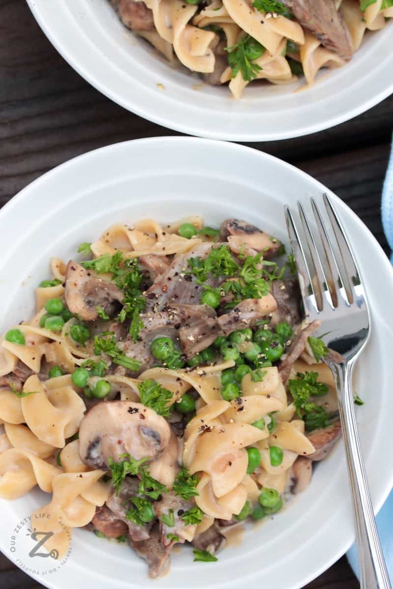 Beef stroganoff with mushrooms and peas on a white plate with a fork