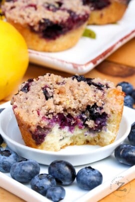 a Blueberry Muffin with Crumb Topping on a white plate with blueberries and muffins on the side