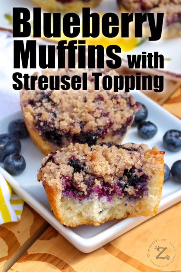 Two Blueberry muffins with streusel topping on plate - one of the muffins is cut in half to see the inside