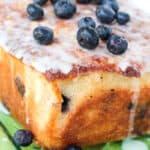 Lemon Blueberry Loaf topped with glaze and berries on a clear plate