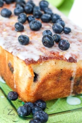 Lemon Blueberry Loaf topped with glaze and berries on a clear plate