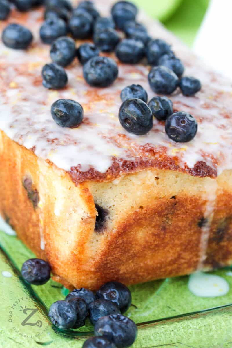 Whole loaf of lemon blueberry on top of a plate with glaze and blueberries on top of the loaf