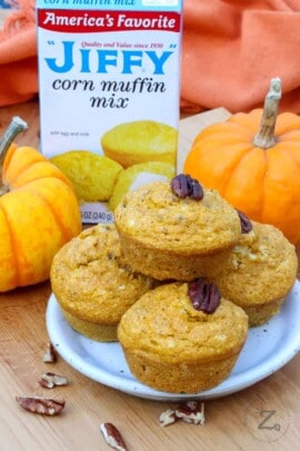a plate of Pumpkin Cornbread Muffins with nuts on them with Jiffy Corn Muffin Mix and pumpkins in the background