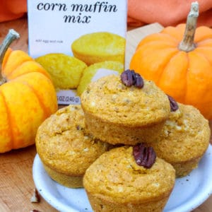 a plate of Pumpkin Cornbread Muffins with nuts on them with Jiffy Corn Muffin Mix and pumpkins in the background